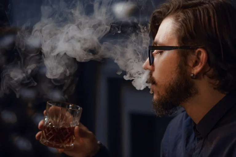 long-haired-hipster-emits-thick-cigarette-smoke-man-holding-glass-with-alcohol-scaled